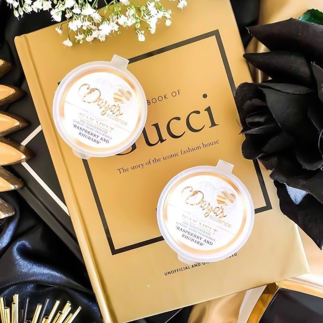 Two Daya's Essence wax melts labeled "Raspberry and Rhubarb" sit atop a gold book about the iconic fashion house Gucci, suggesting a luxurious and sophisticated fragrance experience, read our blog on Wax Melts and Why Curing Matters - Dayas Essence