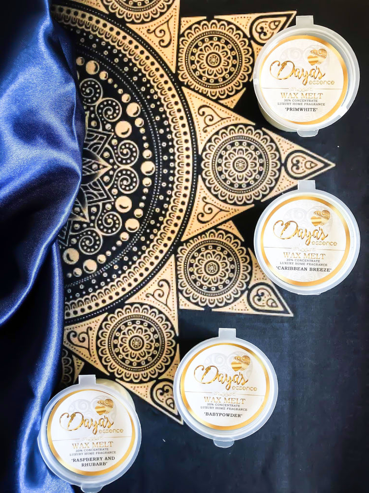 Four Daya's Essence wax melts in various scents, including Caribbean Breeze, Baby Powder, Raspberry and Rhubarb, and Primwhite, displayed on a blue and gold fabric background.