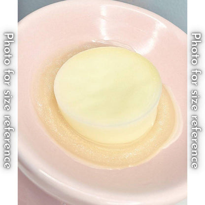 A single, round wax melt sits in a pink ceramic wax melter. The wax melt is slightly smaller than the melter's basin and is surrounded by a pool of melted wax.