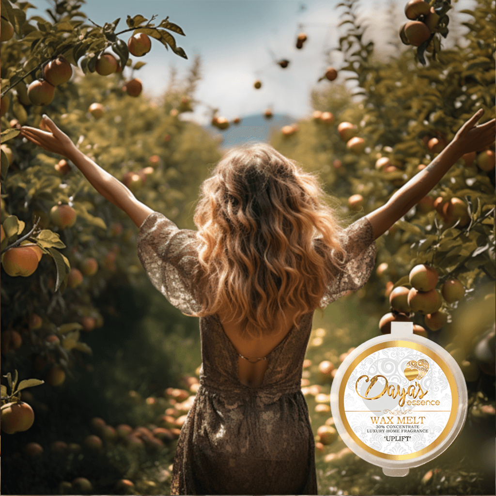 A woman joyfully stands in an apple orchard, her arms outstretched, basking in the beauty of nature's embrace. Forefront a round Dayas Essence wax melt pot with the name uplift on the front