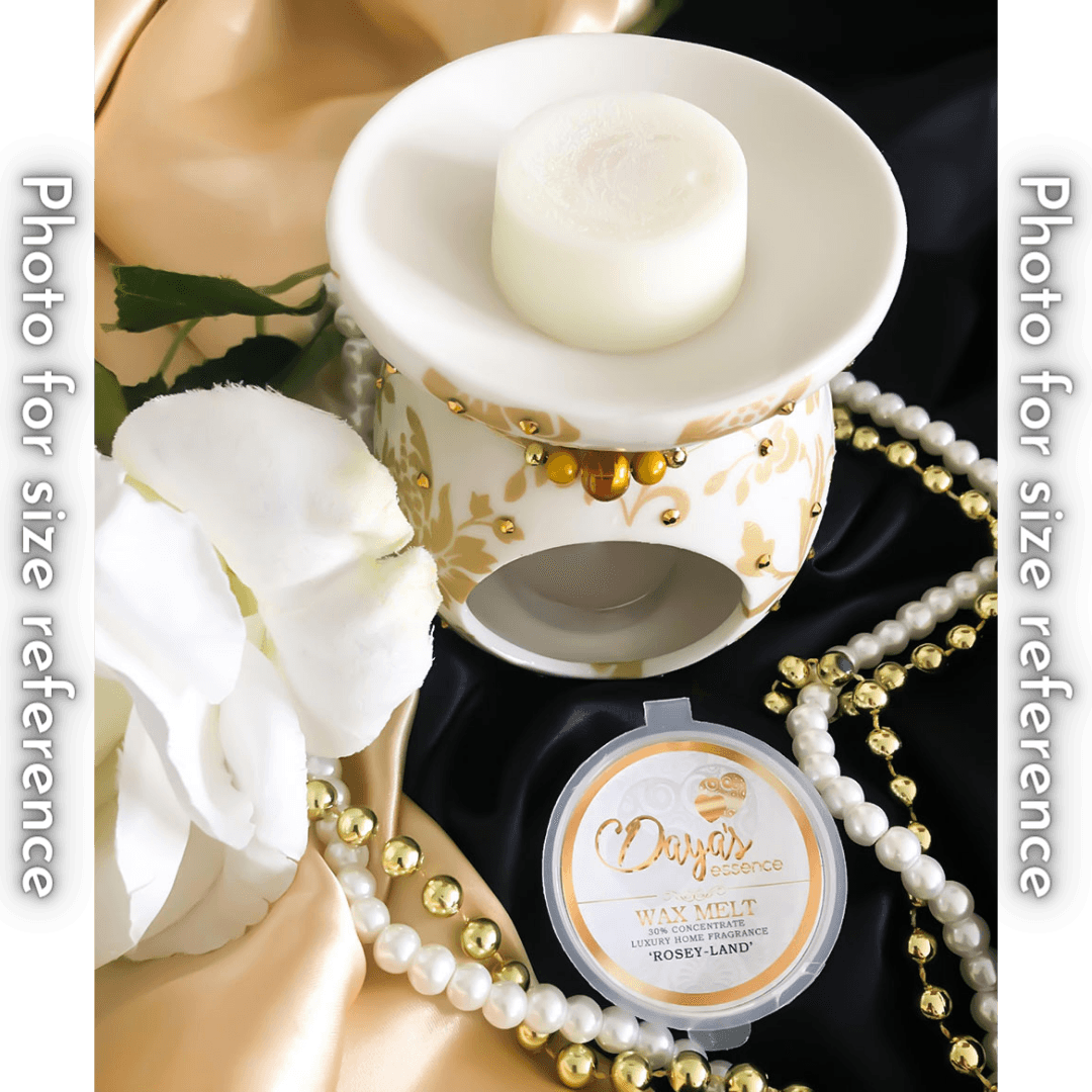 A white ceramic wax melt warmer with a gold and white floral design holds a single white wax melt. The warmer is sitting on a silky fabric next to a string of pearls. A second wax melt, labeled "Rosey-Land" is in its packaging in the foreground.