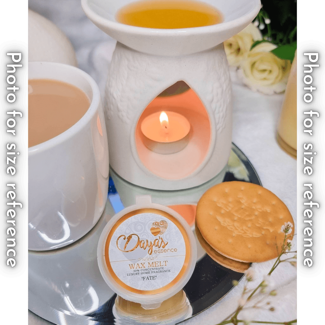 A white ceramic wax melt warmer with a tea light candle and melted wax sits next to a cup of coffee and a Daya's Essence wax melt labeled "Fate." A round cracker is placed in front to show the size of the wax melt.