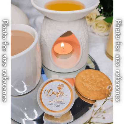 A white ceramic wax melt warmer with a tea light candle and melted wax sits next to a cup of coffee and a Daya's Essence wax melt labeled "Fate." A round cracker is placed in front to show the size of the wax melt.