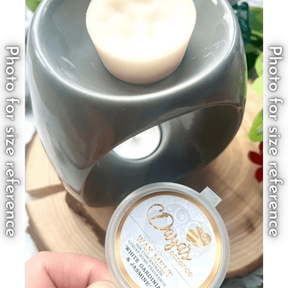 A light grey ceramic wax melt warmer with a white wax melt on top. The wax melt is in a small round plastic container with a label that says "Daya's Essence Wax Melt 30% Concentrate Luxury Home Fragrance 'White Gardenia & Jasmine'."