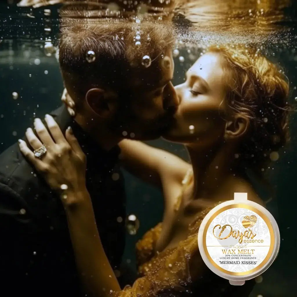 A man and woman kiss underwater, surrounded by bubbles. The woman wears an elegant, sparkling dress and a ring with a large gemstone on her left hand, which rests on the man's shoulder. A circular product label for 'Daya's Essence Wax Melt' with the scent 'Mermaid Kisses' is superimposed in the lower right corner.