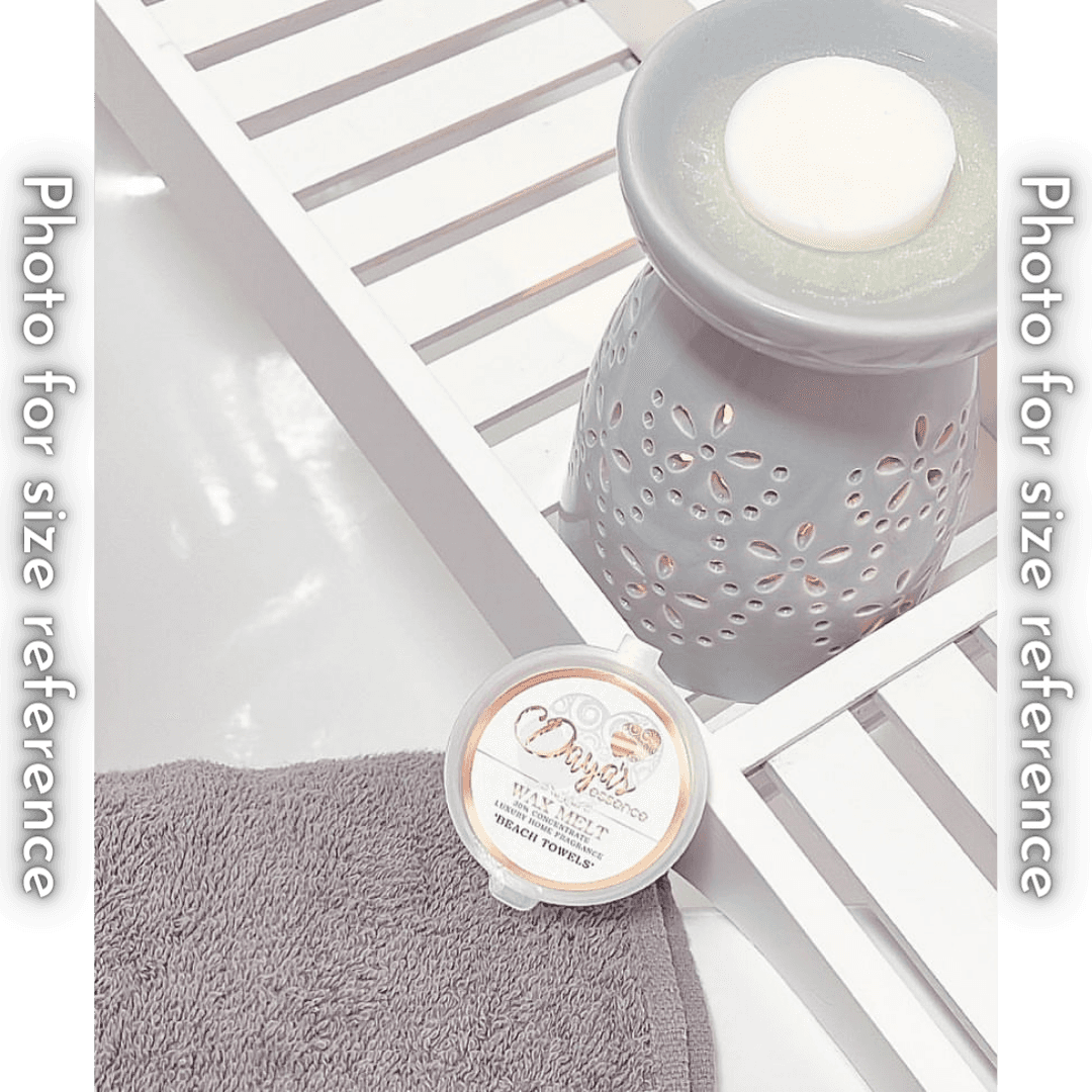 A light grey ceramic wax melt warmer with a white wax melt on top. The warmer sits on a white wooden tray, and a Daya's Essence "Beach Towels" wax melt is placed on a grey washcloth in the foreground.