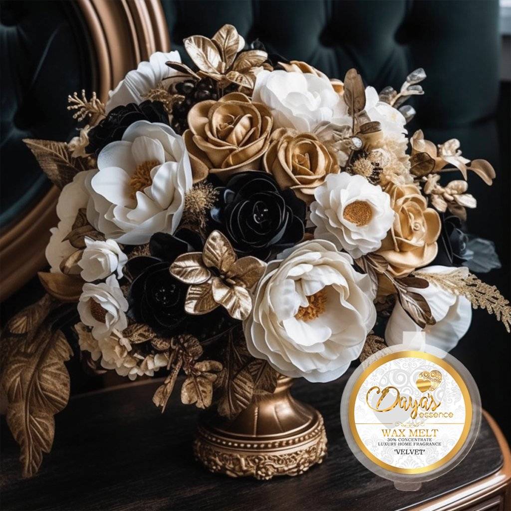 A luxurious "Velvet" wax melt by Days Essence sits on a dark wood surface, nestled amongst a stunning arrangement of black, white, and gold artificial flowers overflowing from a gold urn.